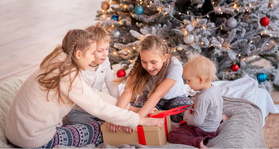 Kids opening a gift in the living room near a Christmas tree.